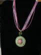 médaillon en broderie parme, jaune et rose soutenu sur tissu vert, cordon organdi et coton ciré parme. Diamètre 30mm. longueur 42cm;