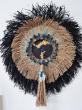 En son coeur une base sombre texturée et mise en lumière par des feuilles d’or, encadrée d’un cercle ornemental composé de coques végétales teintées et de plumes turquoise, formant une couronne vibrante d’énergie. Autour, la corde naturelle rayonne tel un soleil brut, tandis que le raphia noir, sauvage et puissant forme un halo profond et structurant. Un long pompon central, orné de perles, plumes et d’un petit coquillage, prolonge l’ensemble et lui donne une verticalité tribale et poétique.
Cette oeuvre singulière est pensée comme un totem mural, a la fois décoratif et symbolique. Elle trouvera naturellement sa place dans un salon, une entrée, ou un espace de méditation, apportant caractère, texture et spiritualité.