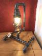 Lampe d'appoint réalisée en tube acier diamètre 22mm et accessoires de plomberie acier et laiton, finition acier brut et application d'un vernis brillant.