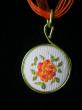 Détail. Médaillon en broderie orange jaune et rouge sur tissu blanc, cordon organdi et coton ciré orange. Diamètre 30mm. longueur 42cm;